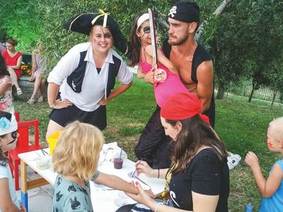 Gruppe Menschen außen, einige verkleidet, sitzen und stehen an einem Tisch mit Bastelmaterial.