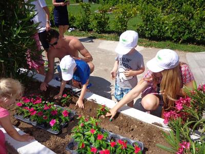 Kinder und Erwachsene pflanzen bunte Blumen in einem Garten mit grünem Hintergrund.
