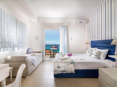 Helles Schlafzimmer mit Meerblick, weiß-blauen Farben, gemütlichem Bett und Sitzbank am Fenster.