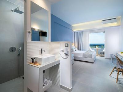 Helles Hotelzimmer mit großzügiger Dusche, Doppelbett, Schreibtisch und Meerblick durch große Fenster.