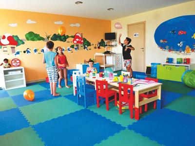 Kindergartenraum mit bunten Spielmatten, kindgerechten Möbeln und Wanddekorationen, drei Kinder spielen.