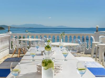 Terrasse mit weiß gedecktem Tisch, blauen Stühlen und Meerblick unter klarem Himmel.
