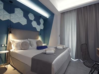 Modernes Schlafzimmer mit Doppelbett, grauen Wänden, geometrischer Wanddeko und schwarzen Stühlen.