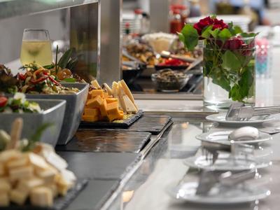 Buffet mit Käse, Salat, Gläsern und roter Rosen-Dekoration auf glänzendem Thekenrand.