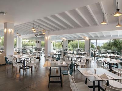 Modernes Restaurant mit weißen Tischen und Stühlen, großer Fensterfront und Blick ins Grüne.