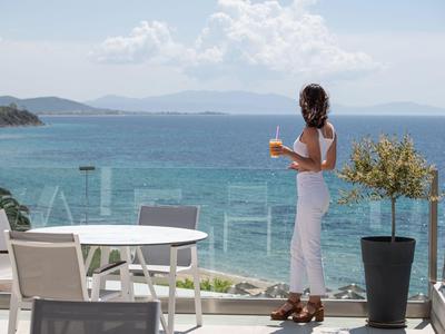 Frau genießt ein Getränk auf der Terrasse mit Blick auf das Meer bei sonnigem Wetter.