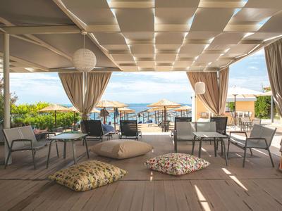 Überdachte Lounge mit Sitzecken und Blick auf den Strand und das Meer.