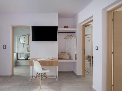 Moderner Hotelraum mit Schreibtisch, Fernseher und offener Garderobe mit Taschen.