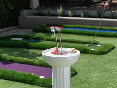 Golfplatz mit Abstellfläche und Golfbällen auf einem weißen Sockel im Vordergrund.