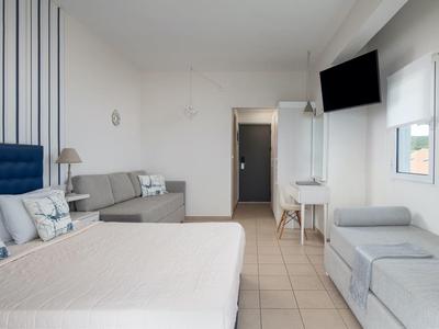Modernes Hotelzimmer mit Doppelbett, Sofa, Schreibtisch und Fernseher an der Wand.