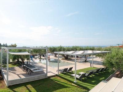 Hotelterrasse mit Liegestühlen, Sonnenschirmen und Blick auf Meer und Berge bei klarem Himmel.