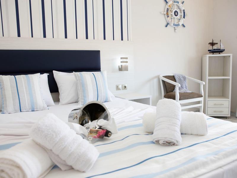 Hell eingerichtetes Schlafzimmer mit weißer Bettwäsche, gestreiften Kissen und maritimen Dekorationen.