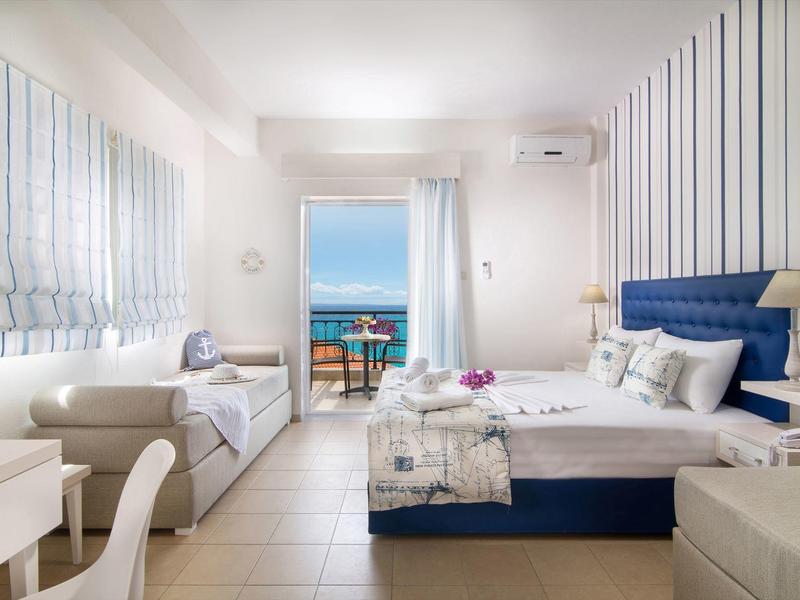 Helles Schlafzimmer mit Meerblick, weiß-blauen Farben, gemütlichem Bett und Sitzbank am Fenster.