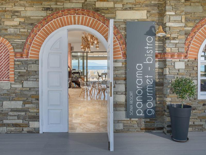 Steinwand mit rundem Bogen, weißer Tür, Banner ?panorama gourmet bistro? und Topfpflanze.