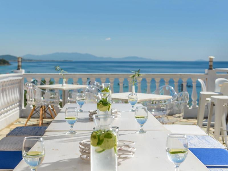 Terrasse mit weiß gedecktem Tisch, blauen Stühlen und Meerblick unter klarem Himmel.