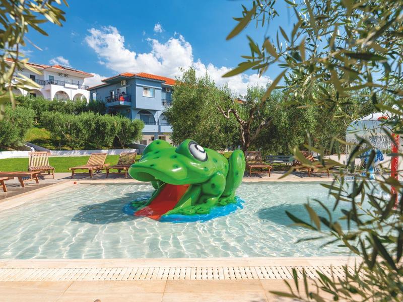 Kleines Kinderbecken mit grünem Frosch-Wasserspiel in sonnigem Garten mit Liegestühlen und blauem Himmel.