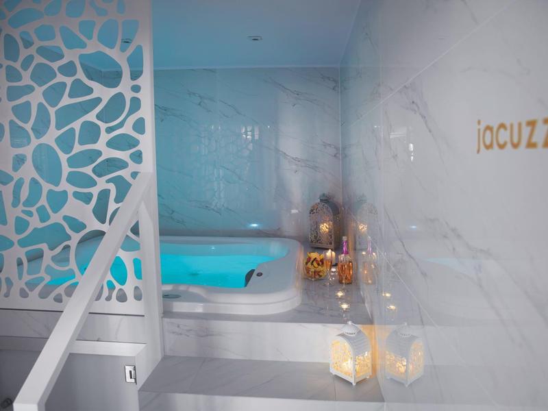 Moderner Wellnessbereich mit beleuchtetem Jacuzzi, dekorativem Sichtschutz und Marmorwänden.