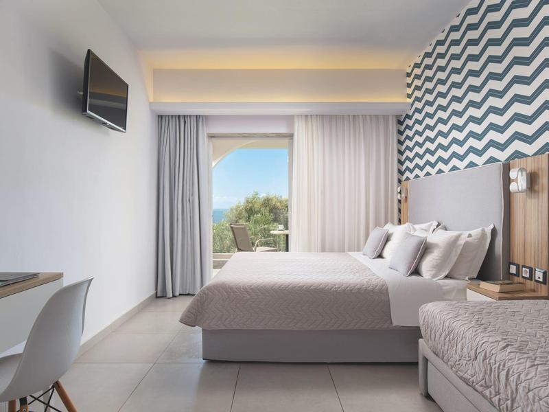 Modernes Hotelzimmer mit Doppelbett, Sesseln und Zugang zu einem Balkon mit Meerblick.