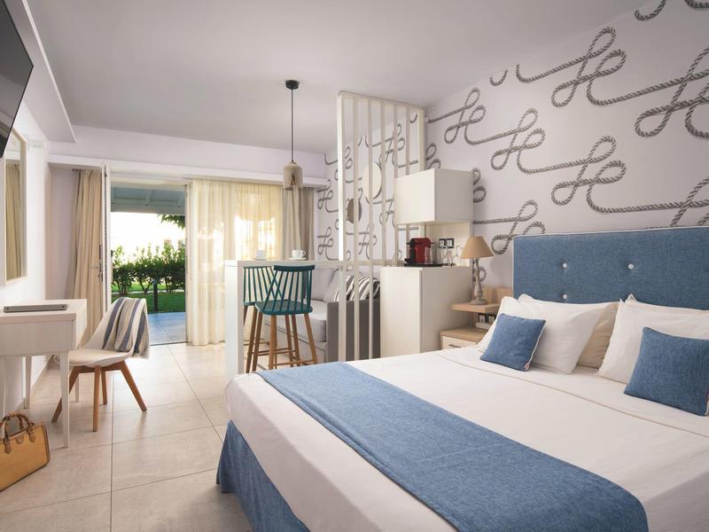 Helles, modernes Schlafzimmer mit blauem Bett, Akzentkissen, Schreibtisch und Zugang zur Terrasse.