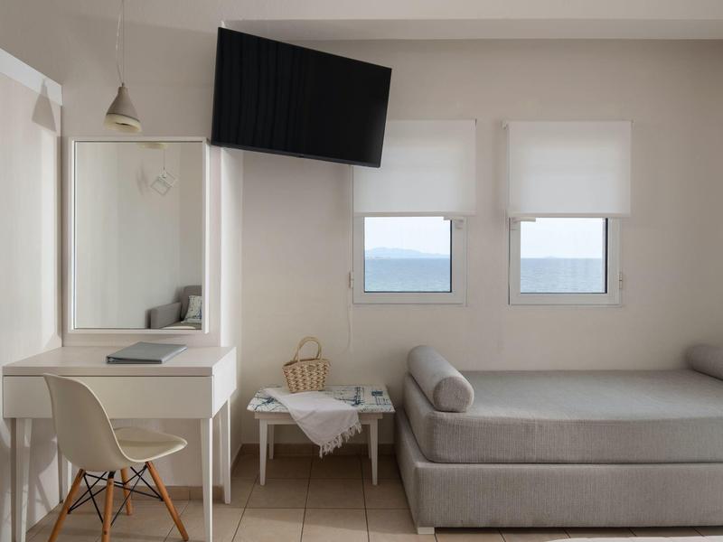 Modernes Hotelzimmer mit Bett, Schreibtisch, Wandfernseher und Meerblick durch zwei Fenster.