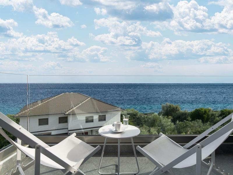 Blick vom Balkon mit zwei Stühlen und einem Tisch auf das Meer und ein Haus.