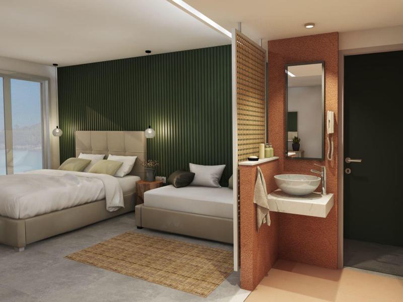 Modernes Hotelzimmer mit Doppelbett, Sessel, grün gestrichener Wand und Bad mit Waschbecken