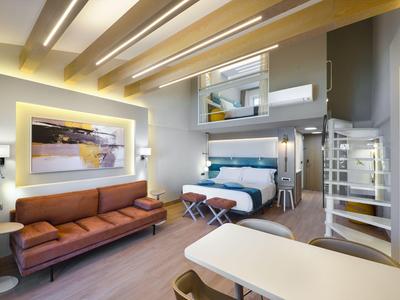 Modernes Hotelzimmer mit hohen Decken, Sofa, Doppelbett und Galerie mit Treppe.