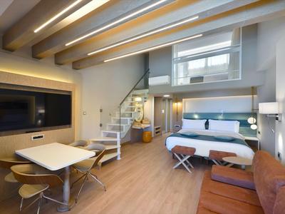 Modernes Hotelzimmer mit Schlafbereich, Sofa, Esstisch und Treppe zur Empore.