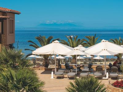 Sonnenterrasse mit Liegestühlen und großen weißen Sonnenschirmen an der Küste mit Blick aufs Meer.