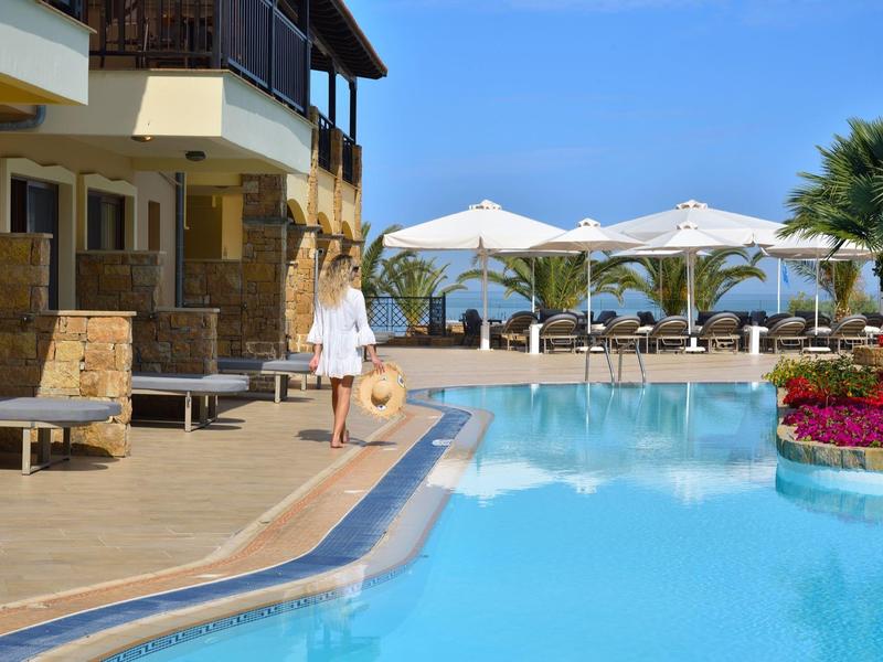 Frau in weißem Kleid am Pool eines Hotels mit Schirmen und Meerblick.
