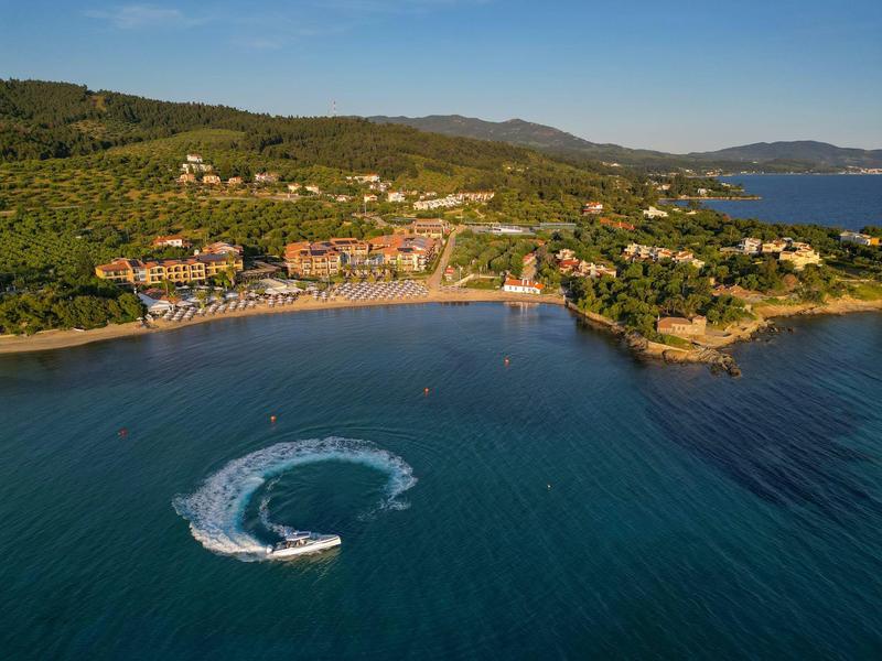 Luftaufnahme eines Küstenresorts mit Sandstrand und Jetboot auf dem Wasser.