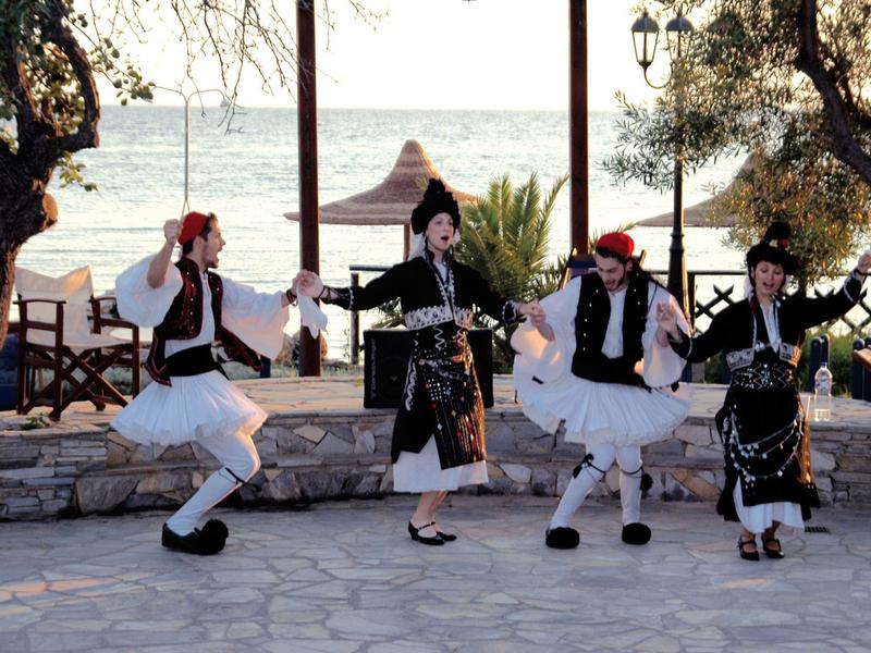Traditionelle griechische Tänzer in Trachten tanzen im Freien am Meer.