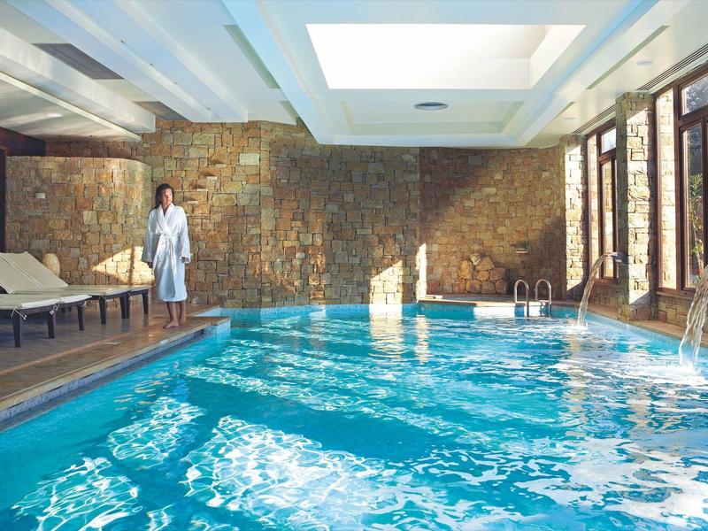 Innenpool mit Steinwand und Liegestühlen, Person im Bademantel steht am Rand