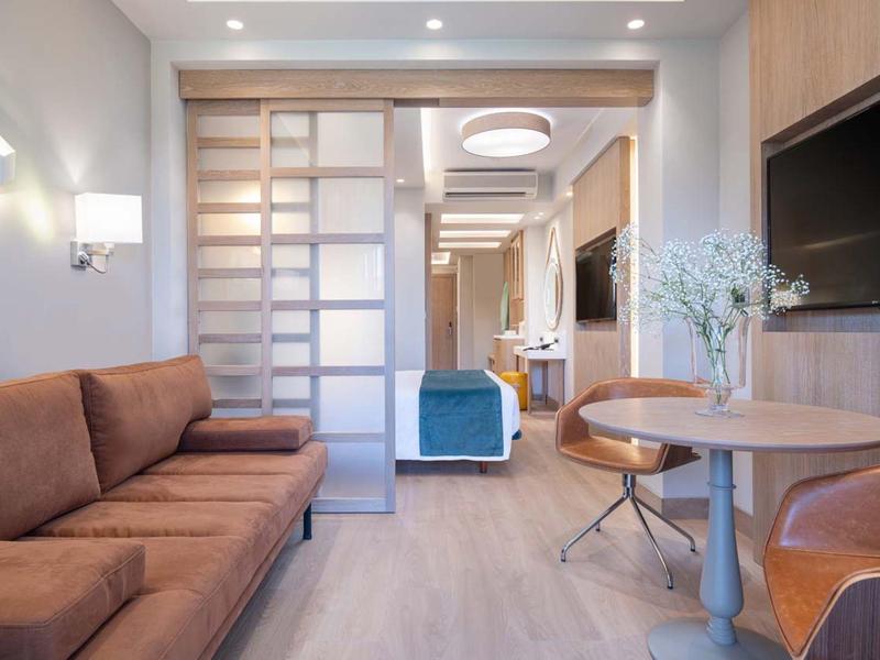 Modern eingerichtetes Wohnzimmer mit braunem Sofa, runden Tischen und Fernseher an der Wand.