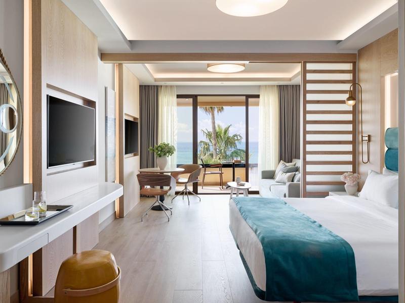 Modern eingerichtetes Hotelzimmer mit Doppelbett, Schreibtisch und Blick auf Meer und Balkon.