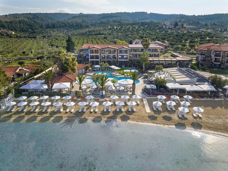 Strandresort mit Liegestühlen, Sonnenschirmen und Pool vor bewaldeten Hügeln