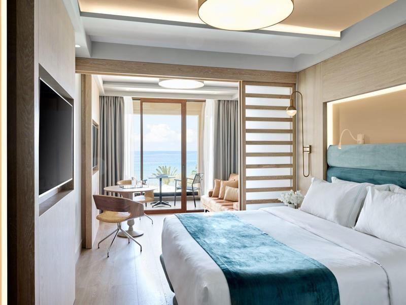 Modernes Hotelzimmer mit Doppelbett, blauem Bettbezug und Blick aufs Meer