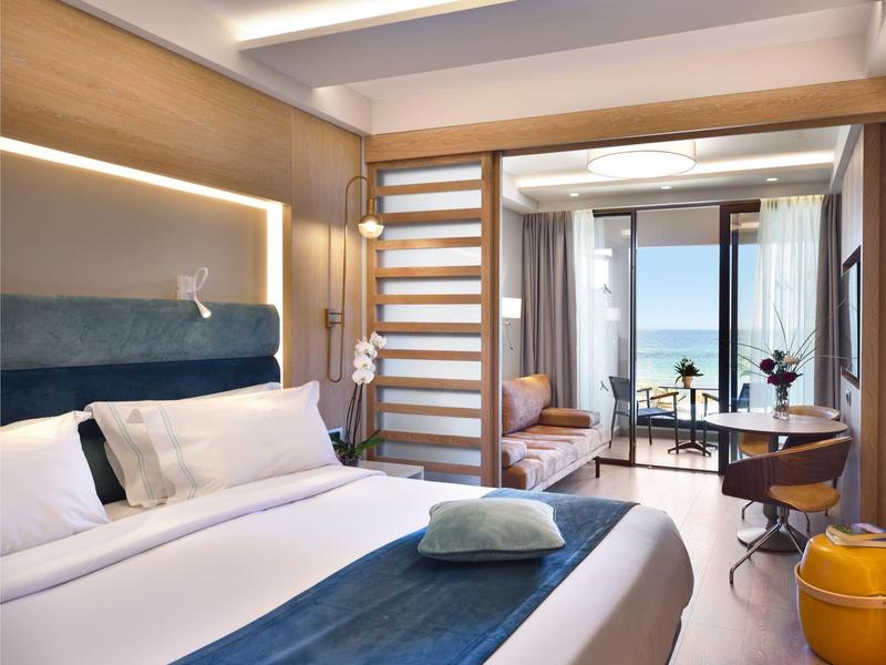 Modernes Hotelzimmer mit Bett, Schreibtisch, Balkon und Blick auf das Meer.