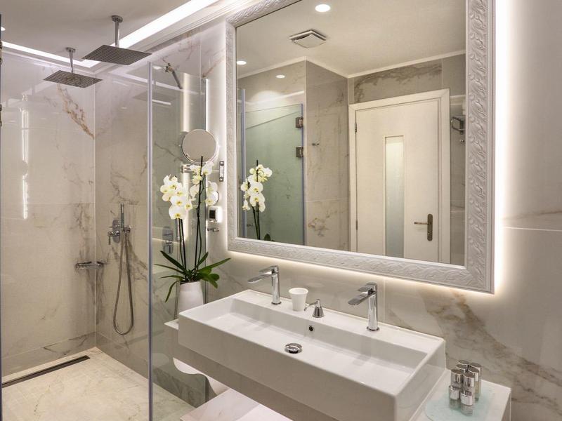 Modernes Badezimmer mit beleuchtetem Spiegel, Doppelwaschbecken und ebenerdiger Dusche.