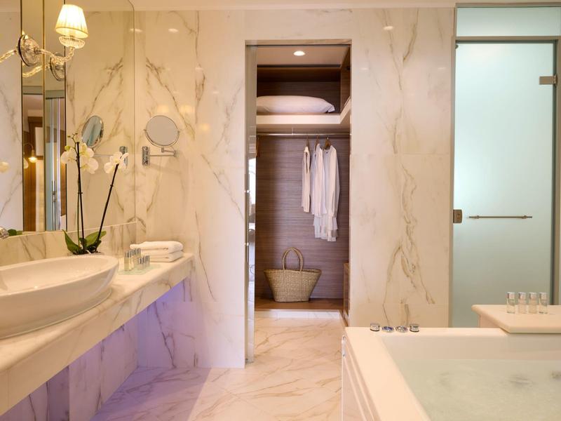 Luxuriöses Badezimmer mit Marmorwänden, Doppelwaschbecken und Badewanne mit Whirlpool-Funktion.