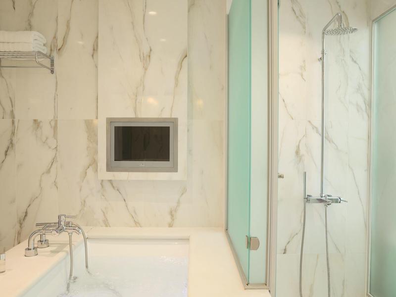 Helles Bad mit Badewanne, eingelassener Dusche und Marmorwandverkleidung.
