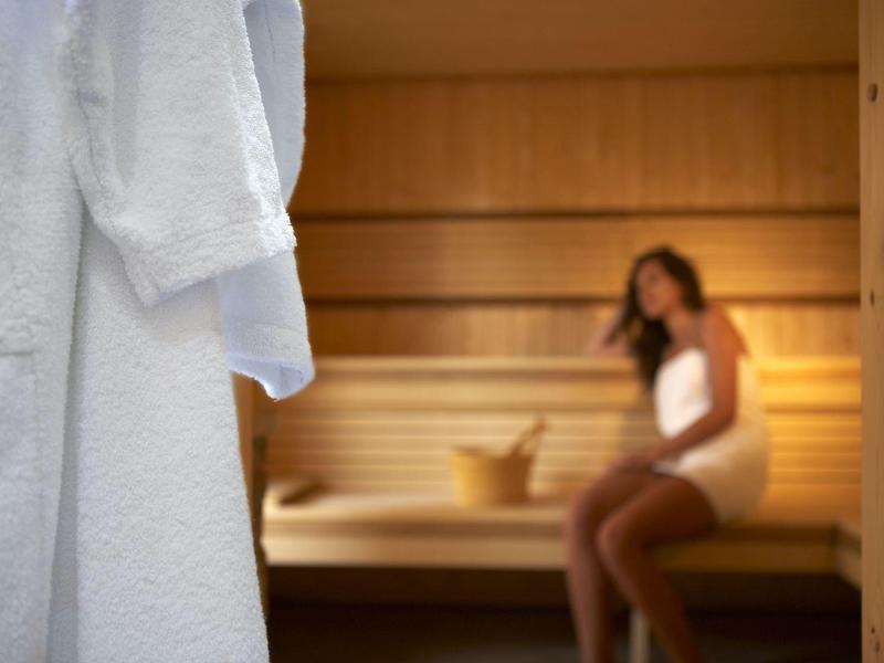 Weißer Bademantel im Vordergrund, unscharfe Frau in Sauna im Hintergrund