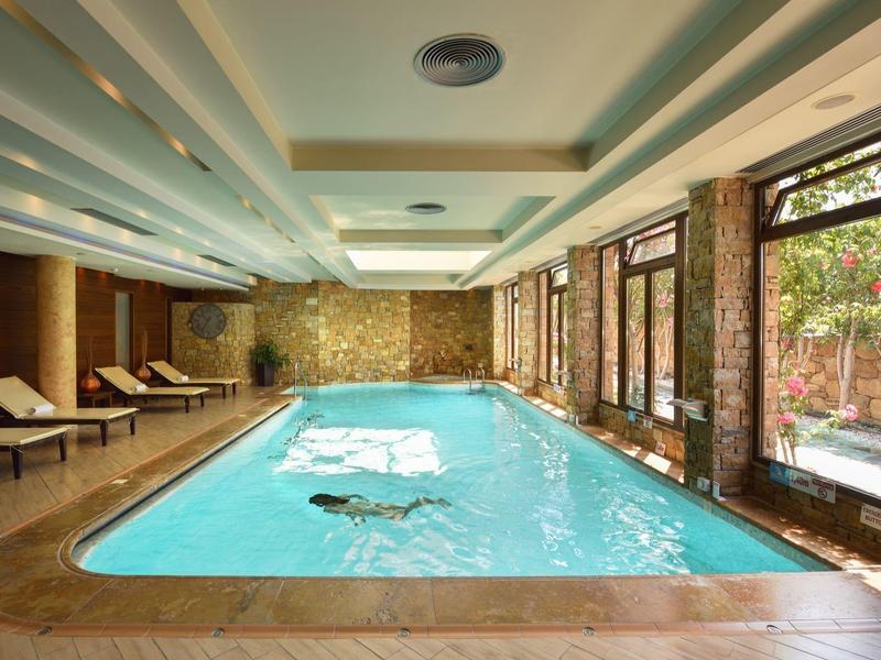 Innenpool mit Liegestühlen und großen Fenstern, die auf einen Garten blicken