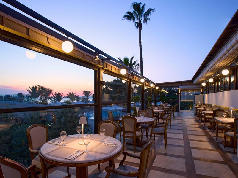Abendlicher Blick auf eine stilvolle Terrasse mit Tischen und Stühlen, umgeben von Palmen.