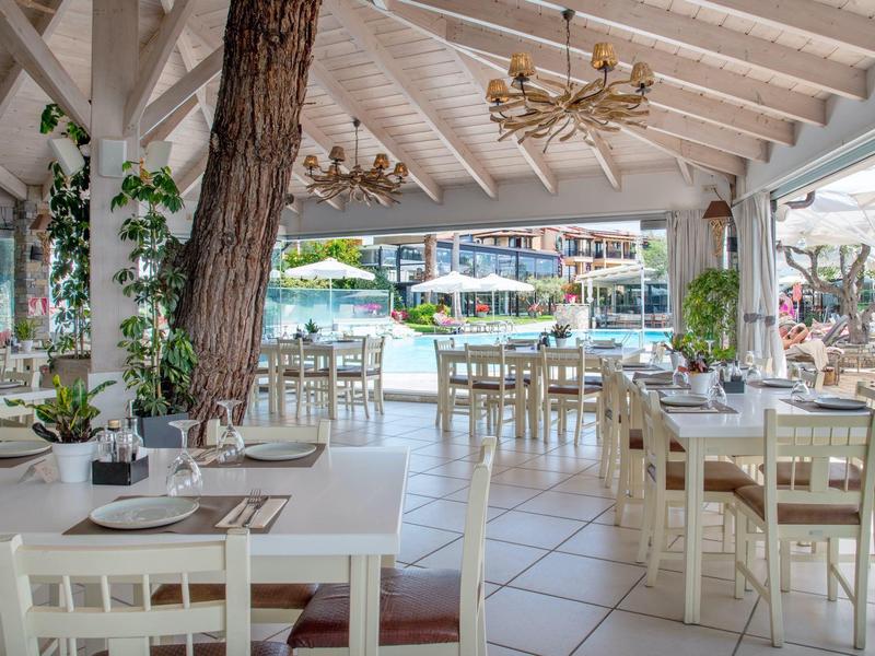 Offenes Restaurant mit weißen Tischen und Stühlen, direktem Blick auf den Poolbereich.