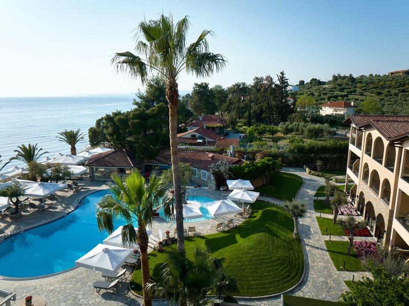 Hotelanlage mit Pool, Palmen und Meerblick bei klarem Himmel.