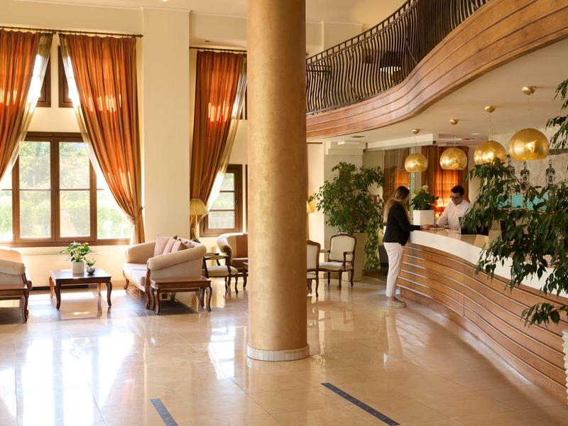 Heller Hotellobby mit großen Fenstern, gemütlichen Sitzbereichen und Rezeption mit Gast.