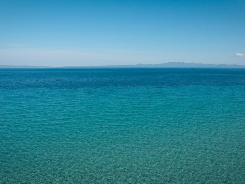 Čisté modré moře pod jasnou oblohou s vzdálenou zemí na horizontu.