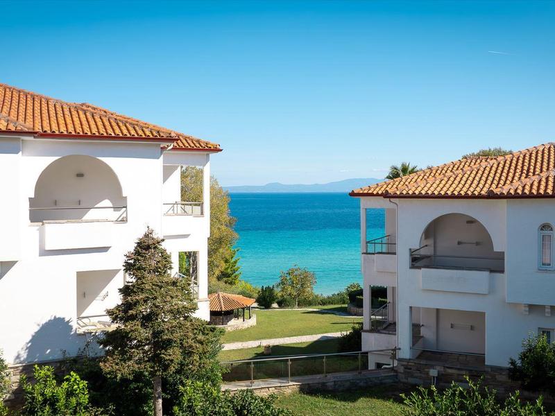 Dvě bílé středomořské vily s červenými střechami s výhledem na modré moře za jasné oblohy.