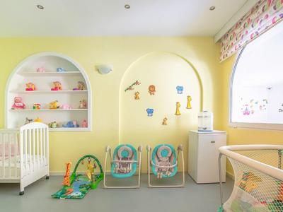 Bright yellow nursery with crib, toys, and two small chairs next to a high chair.